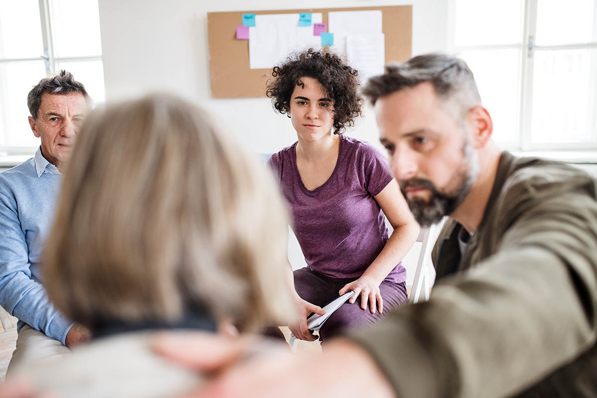 Men and women sitting in a circle during group therapy, supporting each other. a group of people comfort a woman and discuss the signs of alcohol addiction